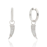 A pair of silver huggie hoop earrings with dangling claw-shaped charms paved with clear stones, shown on a white background with a soft reflection.