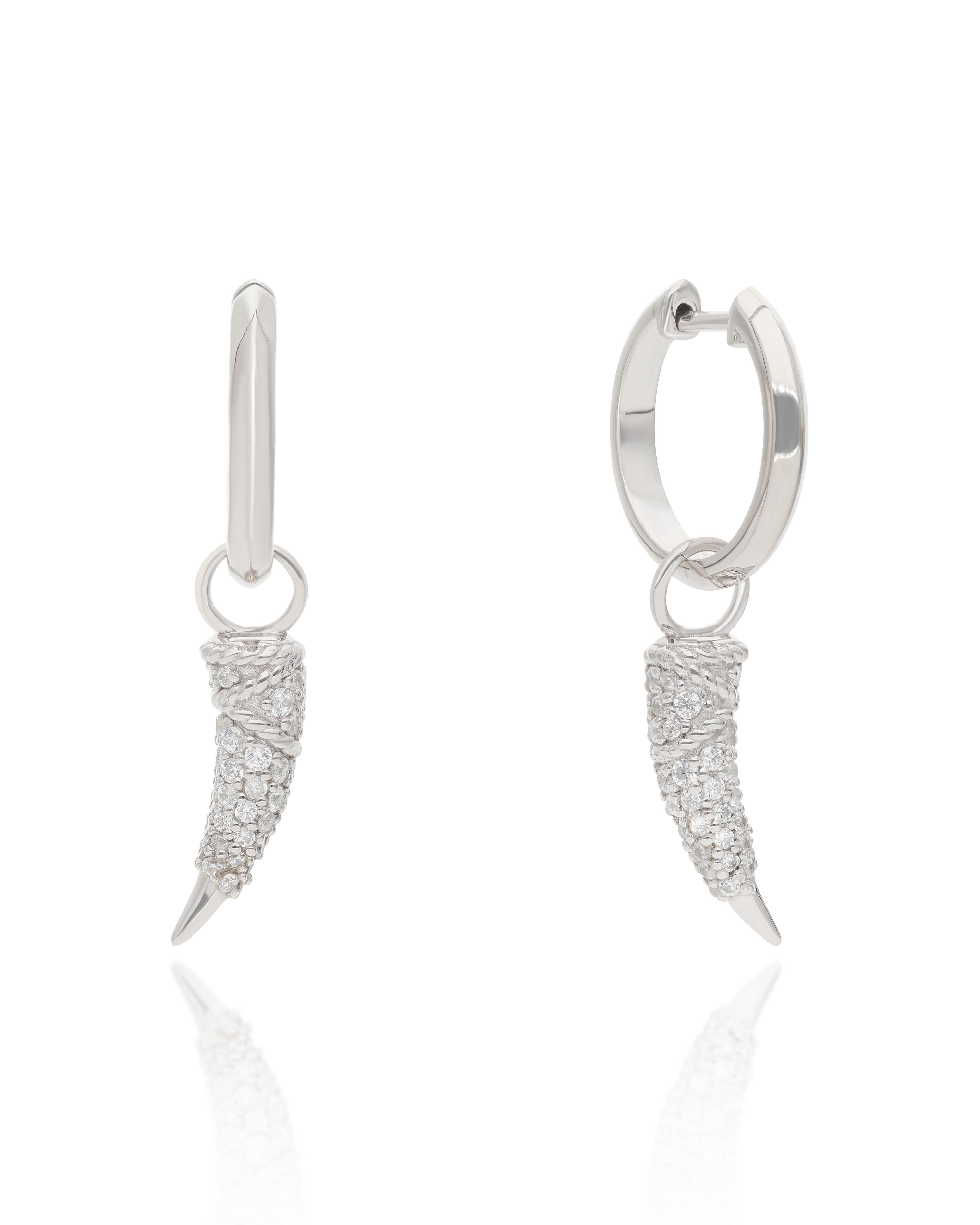 A pair of silver huggie hoop earrings with dangling claw-shaped charms paved with clear stones, shown on a white background with a soft reflection.